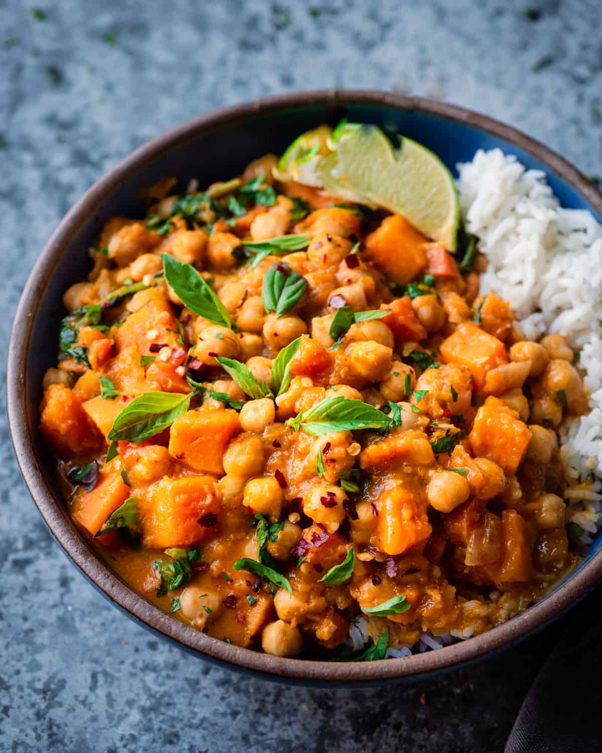 butternut squash curry with chickpeas in a blue cermamic bowl with Thai basil and white rice.