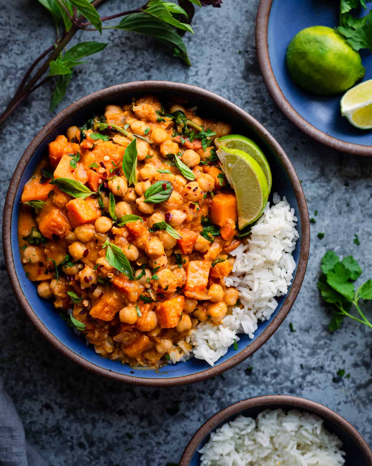 butternut squash curry with chickpeas in a blue ceramic bowl with white rice and lime wedges.