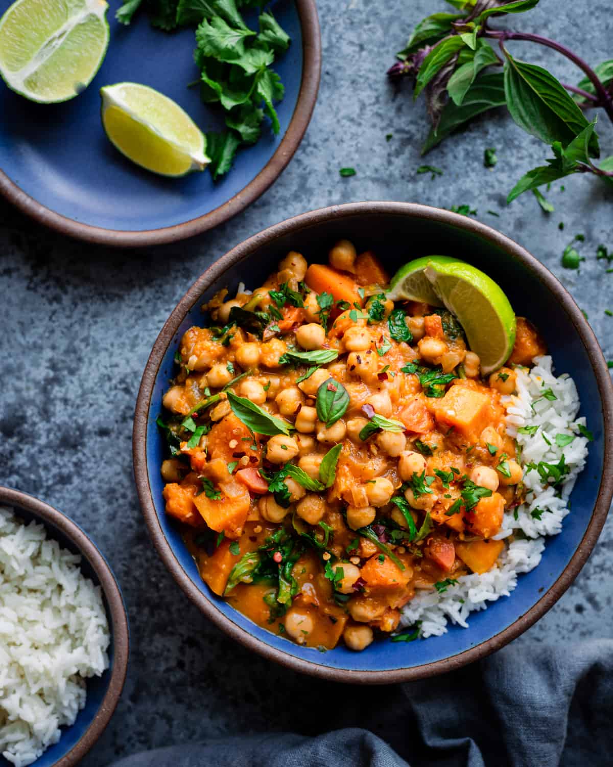 butternut squash curry with chickpeas in a blue bowl with rice and limes on a blue table.