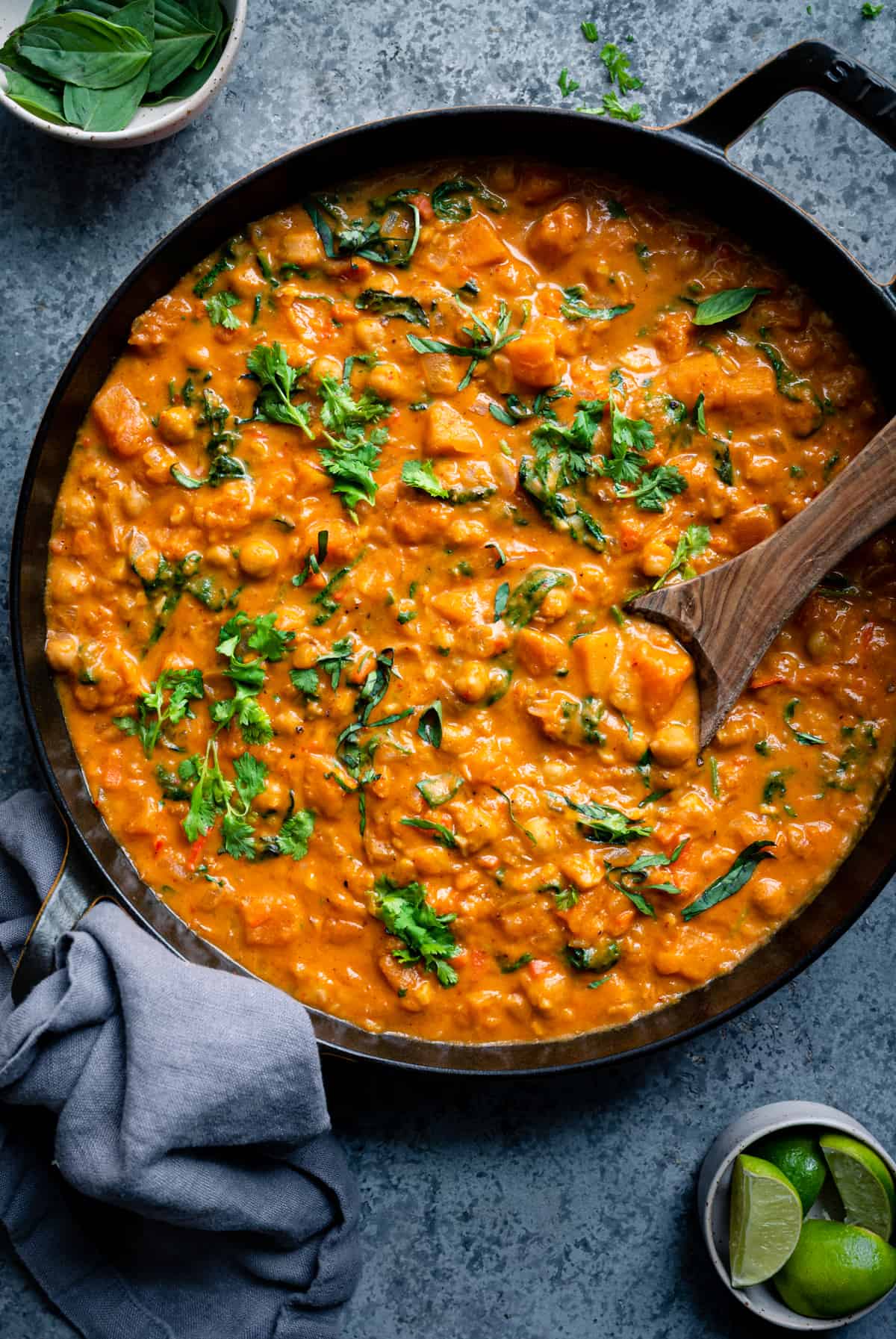 butternut squash curry with chickpeas and greens in a black pan with spoon dug into the curry.