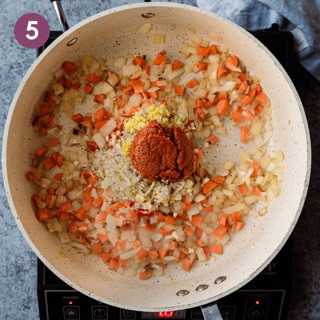 thai red curry paste, lemongrass, ginger and garlic sitting on top of sauteed onions and carrots in a saute pan.