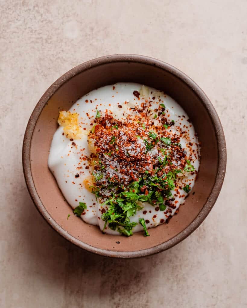 spices, herbs and chopped preserved lemon on top of a bowl of yogurt.