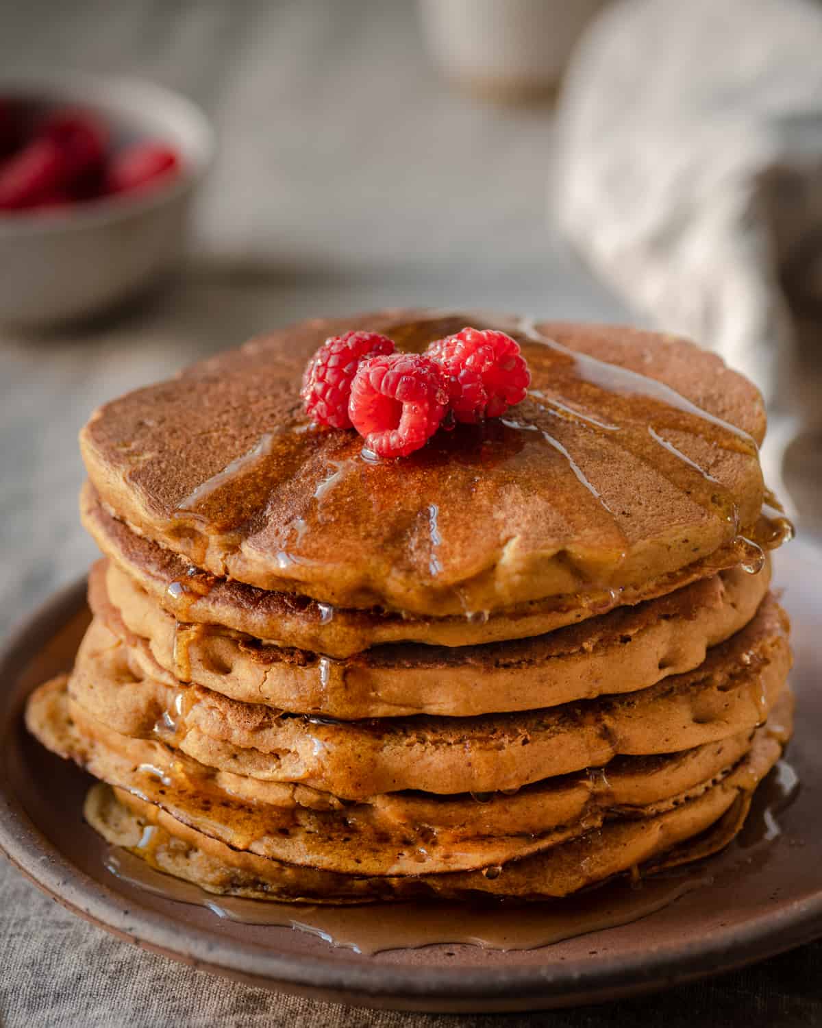 vegan pumpkin pancakes with maple syrup and raspberries on linen tablecloth