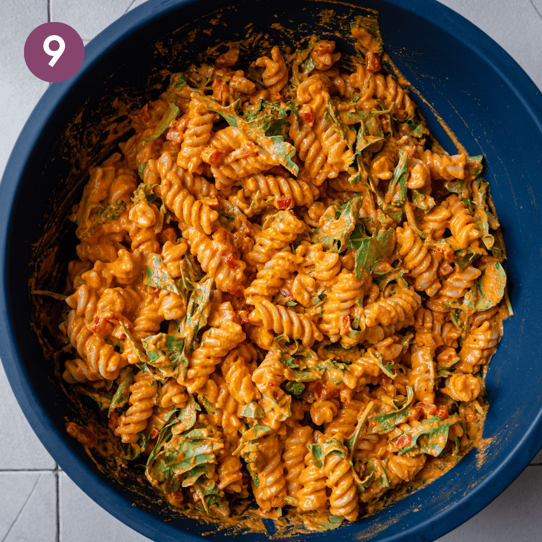 roasted red pepper pasta salad tossed with arugula in a big blue bowl.