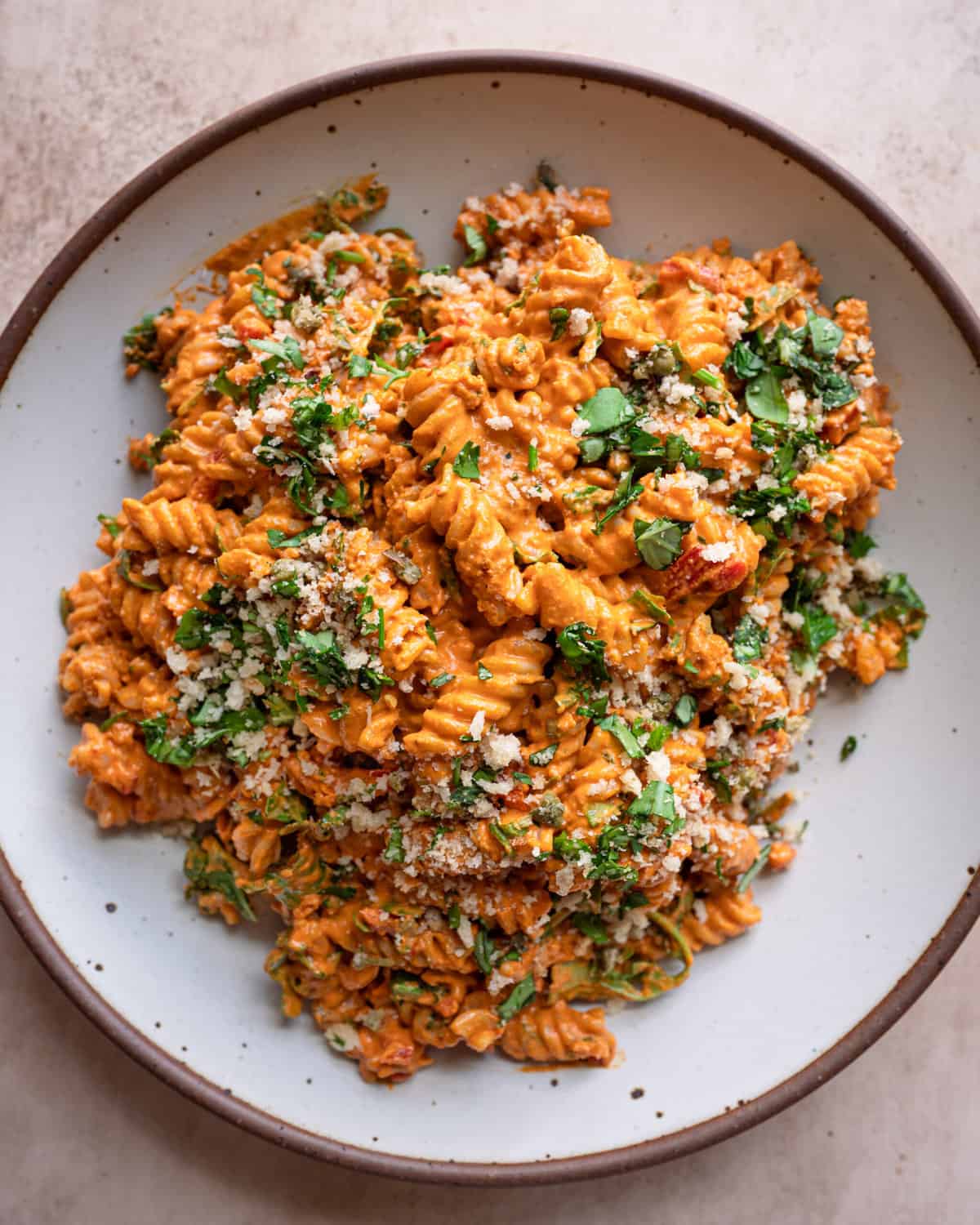 vegan roasted red pepper pasta salad in a speckled white bowl, garnished with basil.