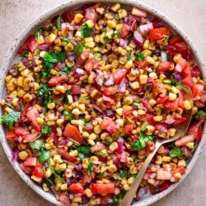 Corn salsa in a shallow white bowl with a spoon.