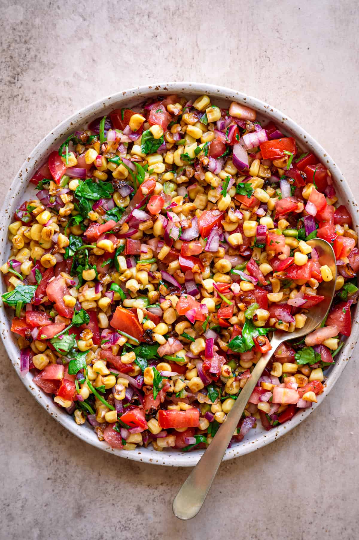 Corn salsa in a shallow white bowl with a spoon.
