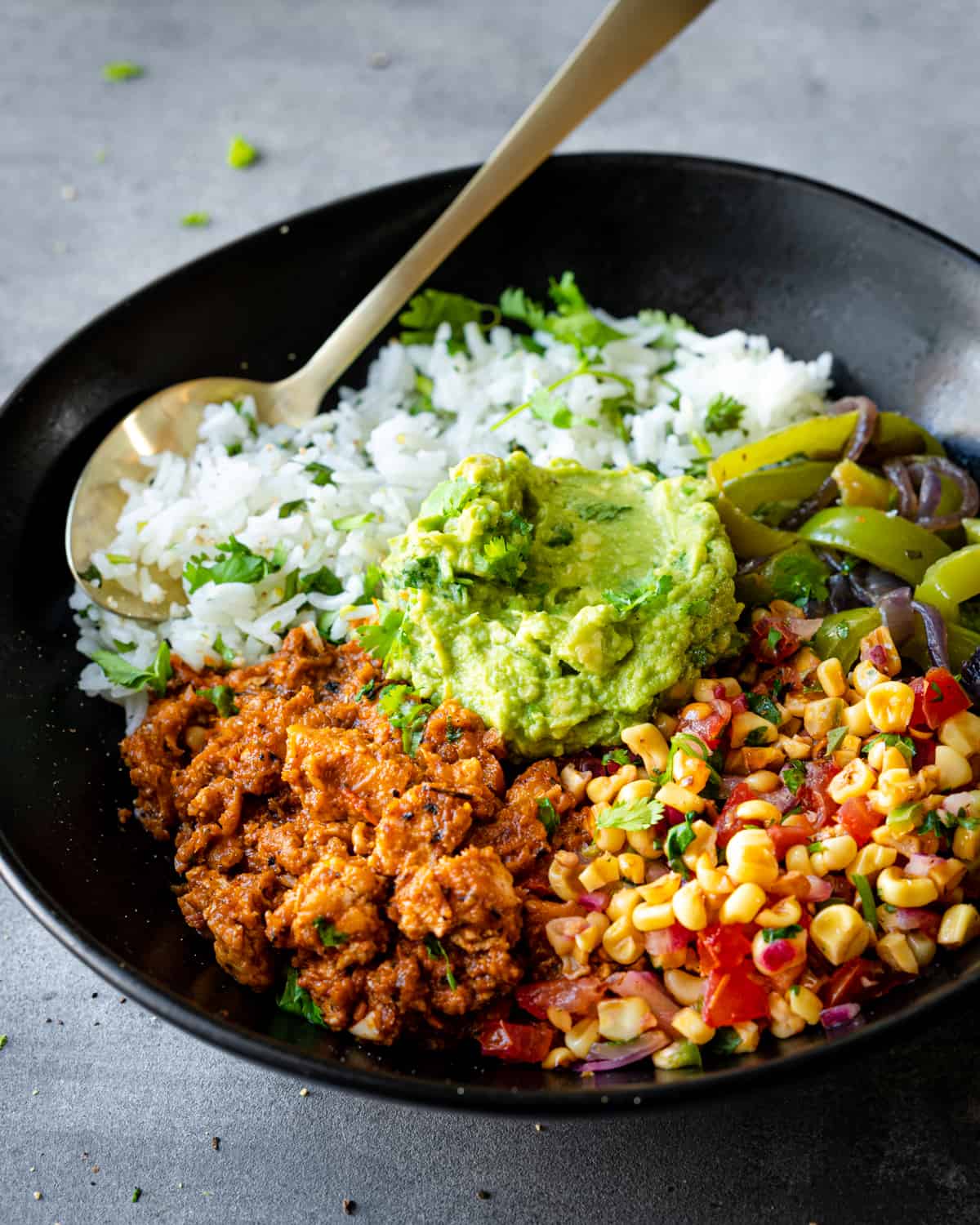 Angled view of burrito bowl components in black bowl with a spoon.