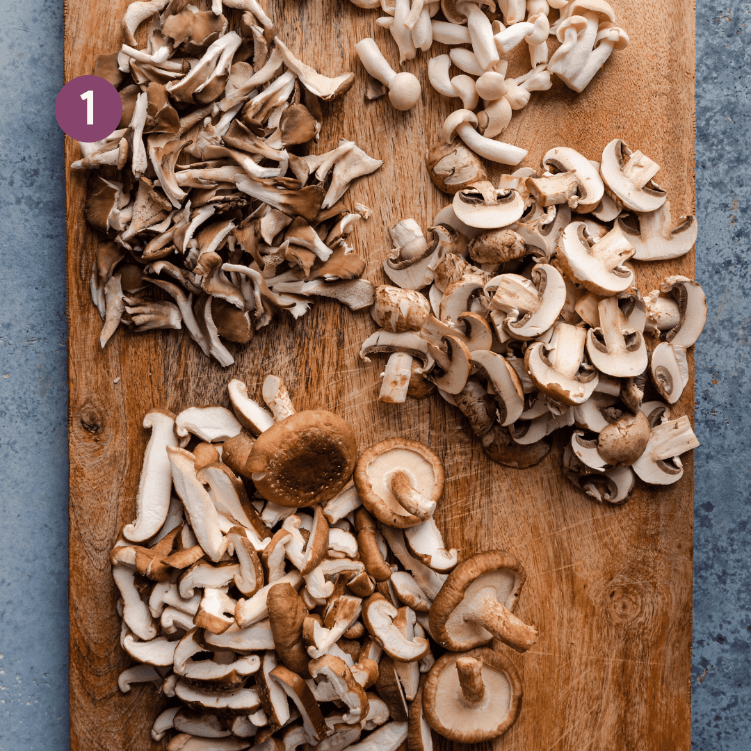 different varieties of mushrooms sliced or torn on a wooden cutting board.