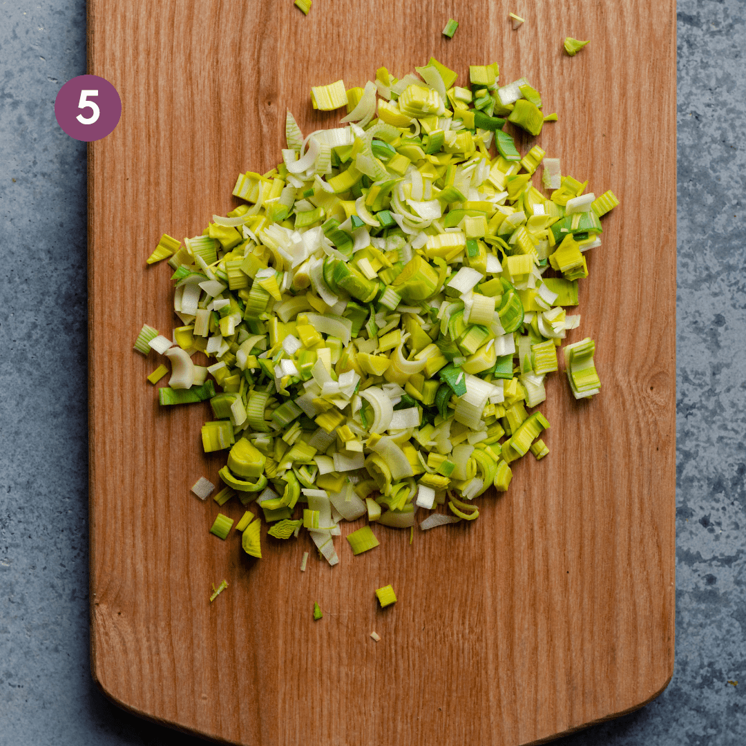 diced leeks on a wooden cutting board on a blue surface.