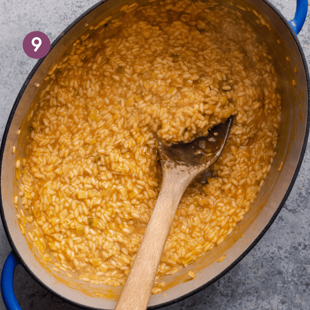 creamy golden vegan risotto in a large dutch oven with a wooden spoon dug into the risotto to show texture.