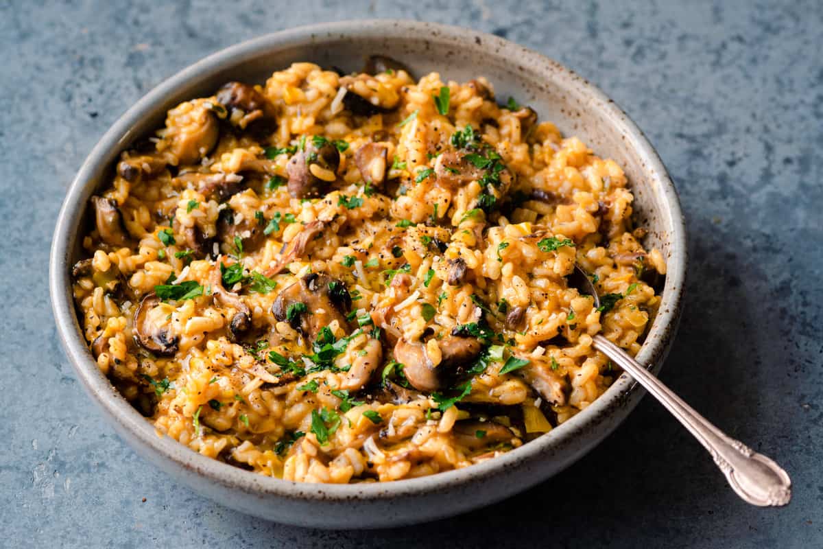 creamy vegan risotto with mushrooms in a ceramic bowl on a blue surface.