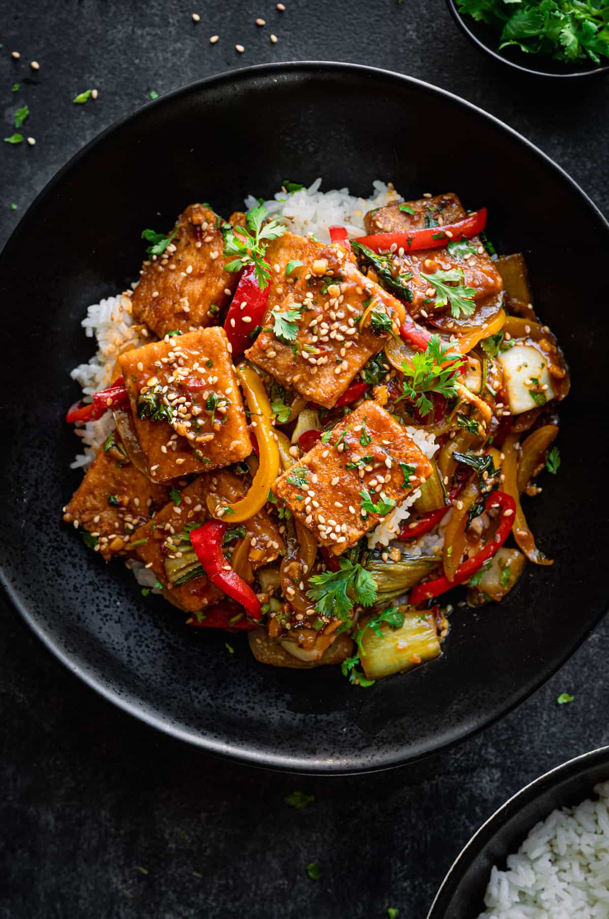 Tofu and pepper stir fry on a bed of white rice in a black bowl.