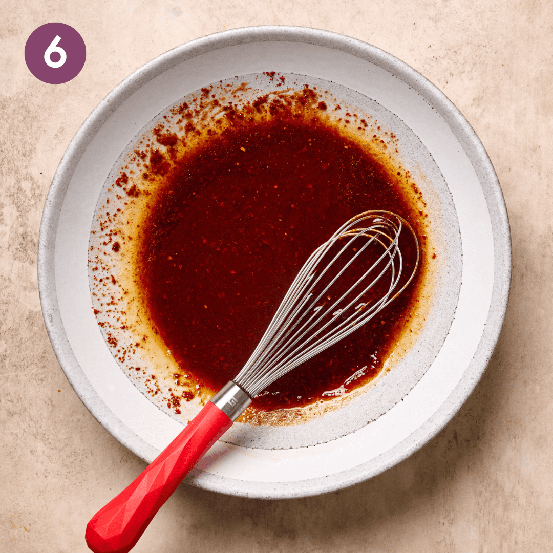 Whisked gochujang sauce with whisk in white bowl.