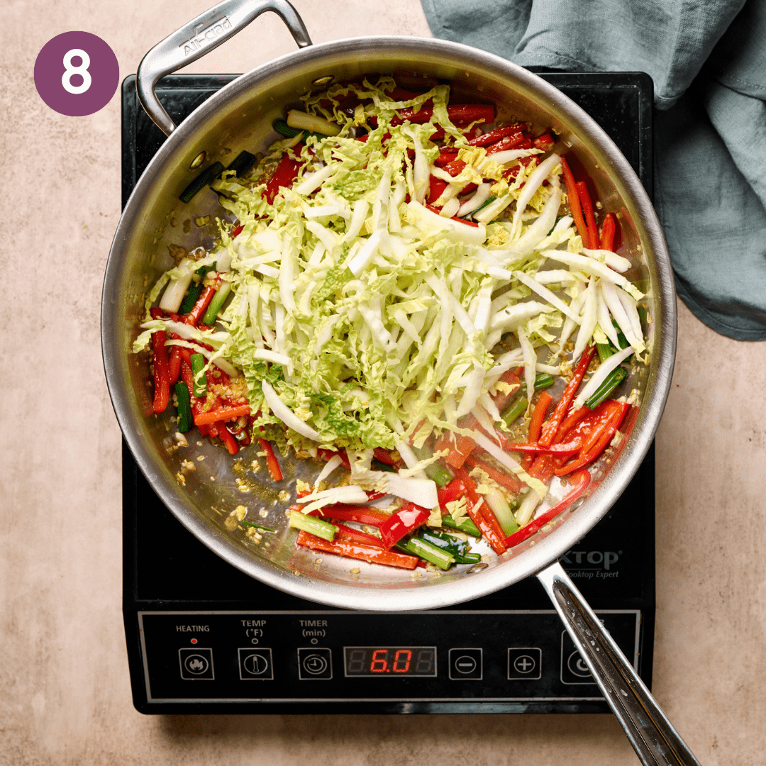 Cabbage added to aromatic vegetable mixture in a pan.