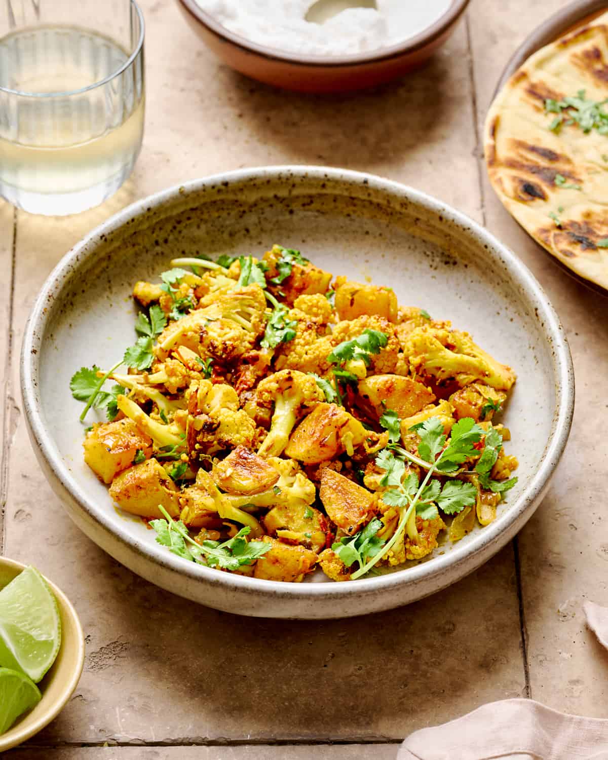 Aloo Gobi in a white bowl on a brown tile table.