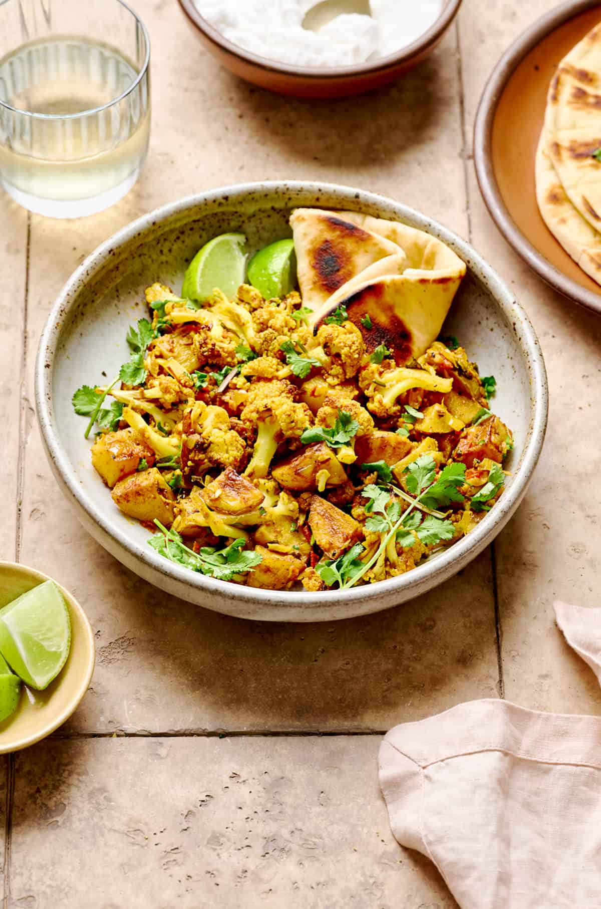 Aloo Gobi with naan in a white bowl on a light brown tiled table.