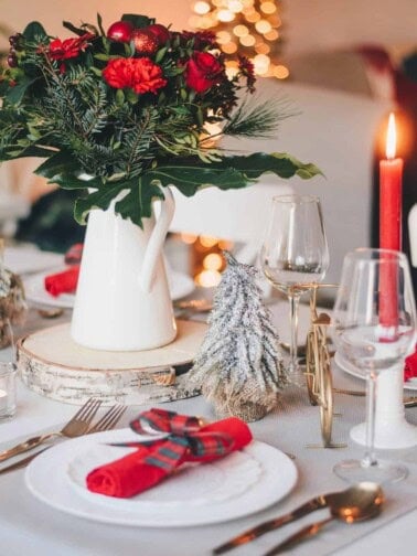 winter holiday table setup with flowers, candles, wine glasses and a tree in the background.