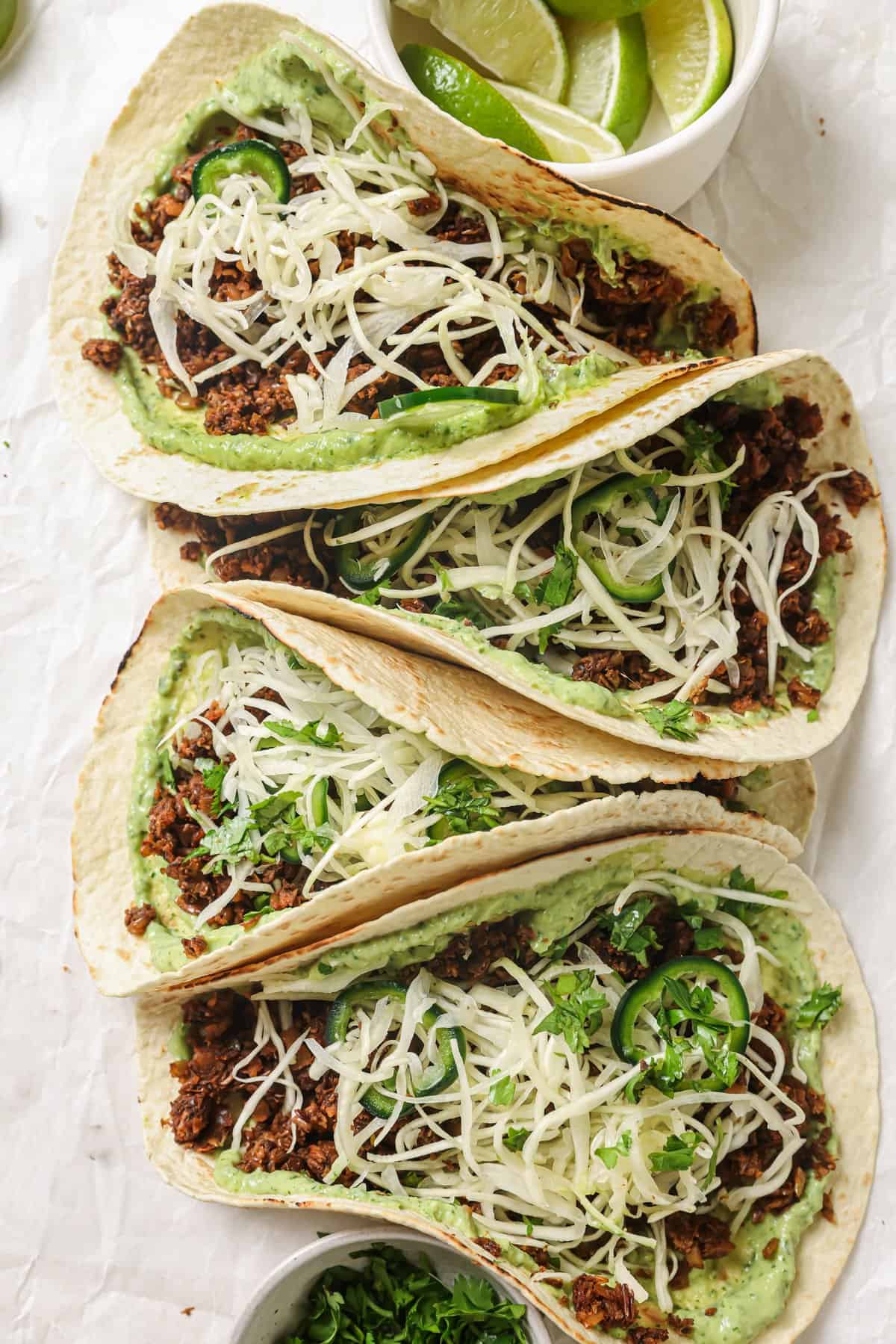 closeup of four lentil tacos with avocado crema and slaw on parchment paper.