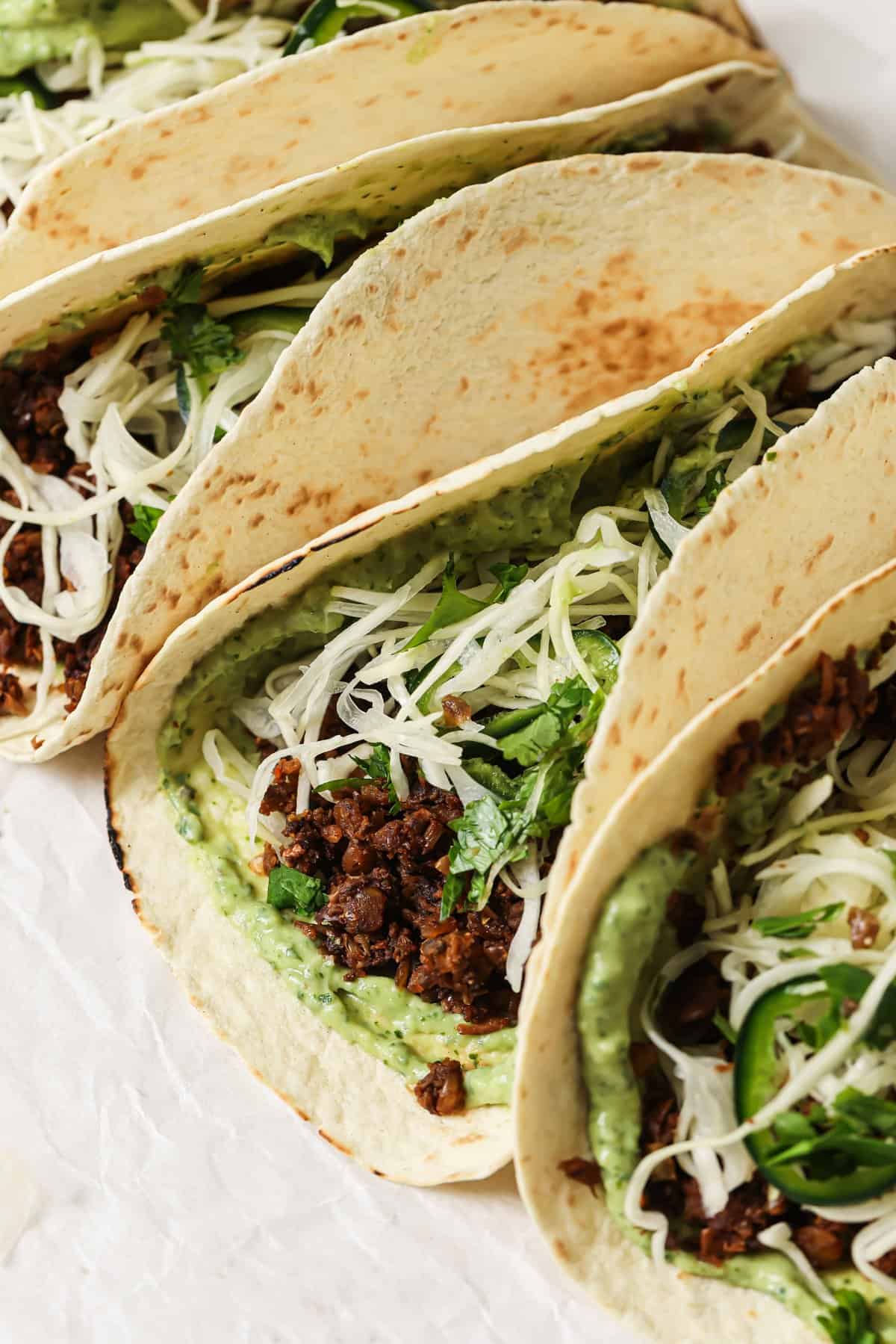 closeup of lentil tacos with avocado crema and slaw on parchment paper.