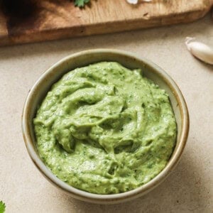 bowl of avocado crema on a table next to a cutting board with ingredients.
