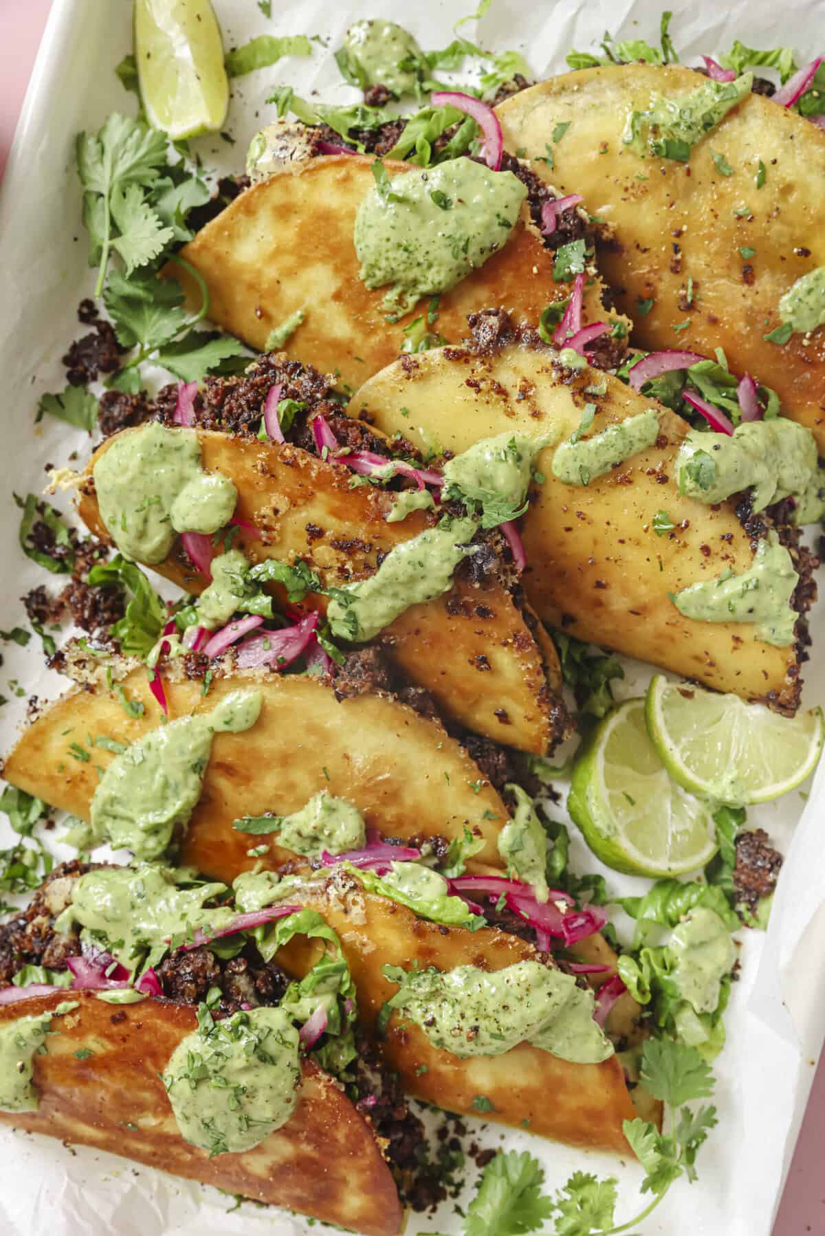 pile of black bean tacos with fillings and avocado crema on top.