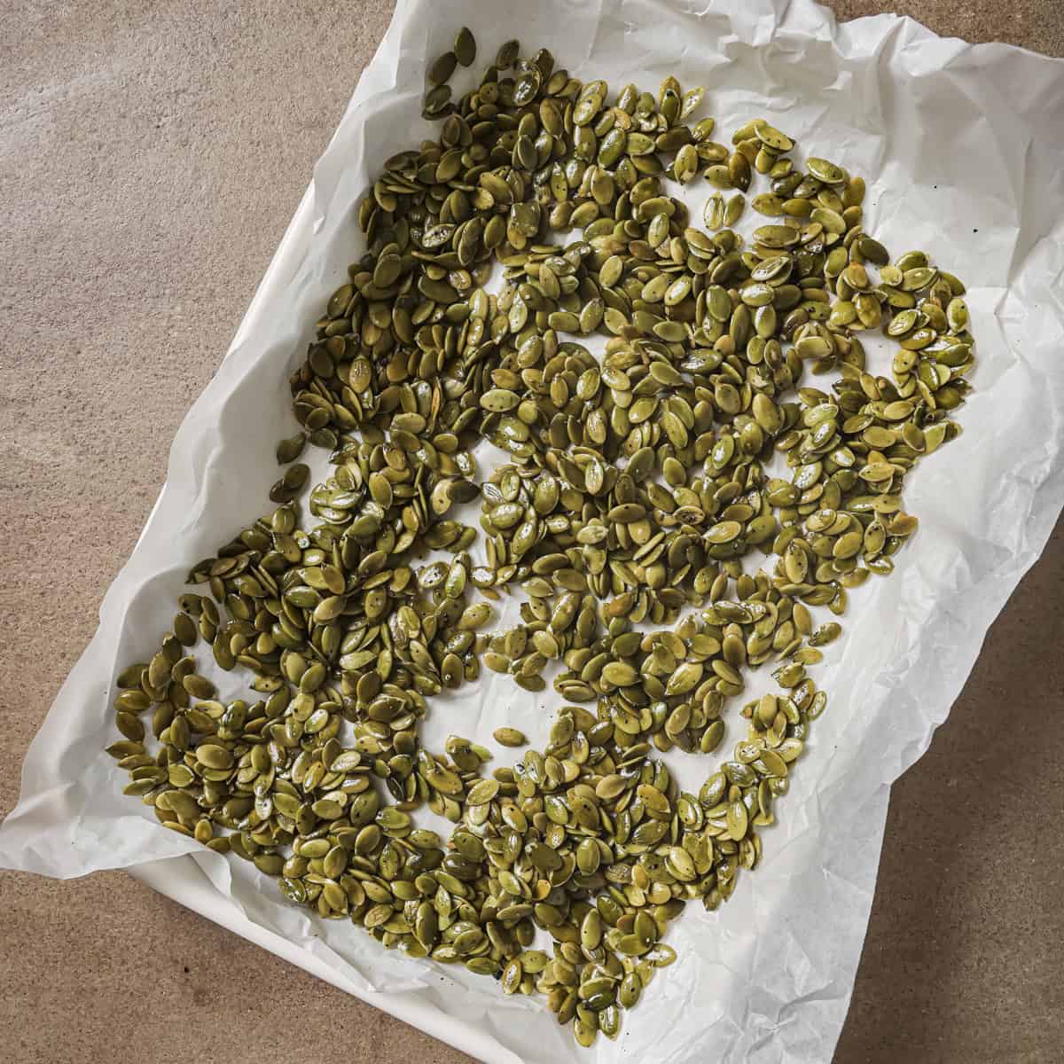unroasted pepitas on a parchment paper lined sheet pan.