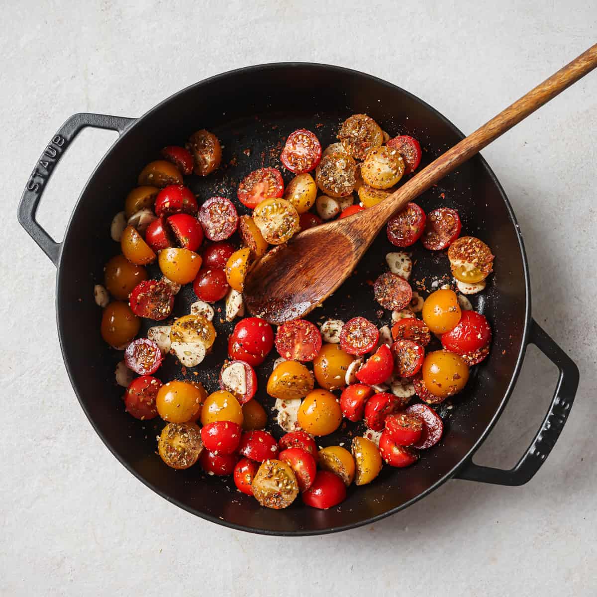 tossed tomatoes and a long wooden spoon in the baking dish.