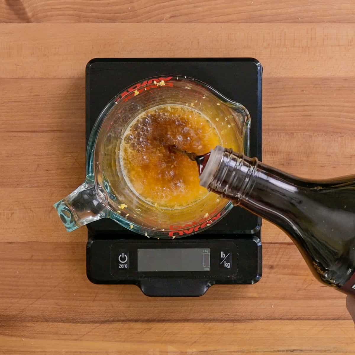 Person combining all orange sauce ingredients in a glass measuring cup.