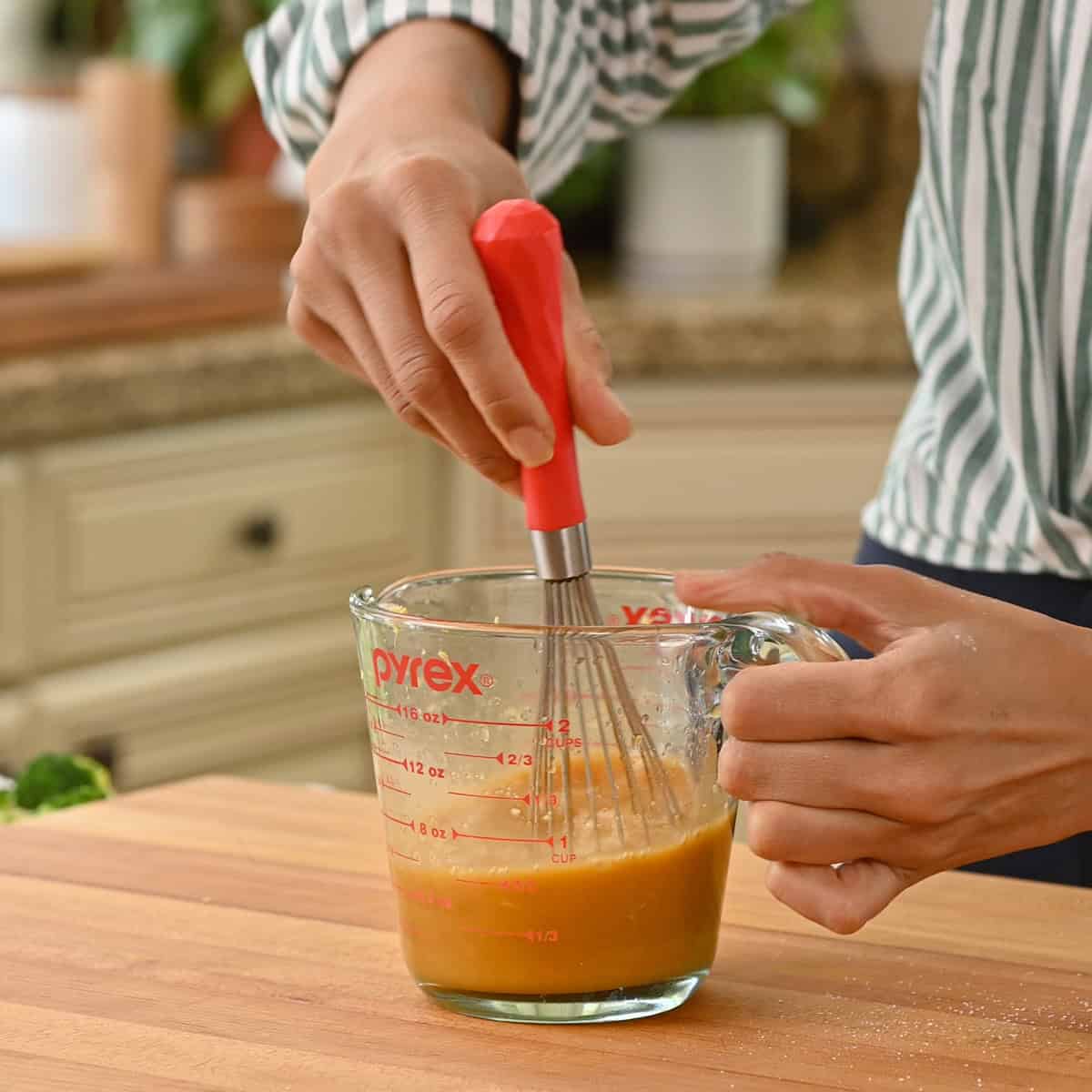 Person whisking orange sauce in a glass measuring cup.